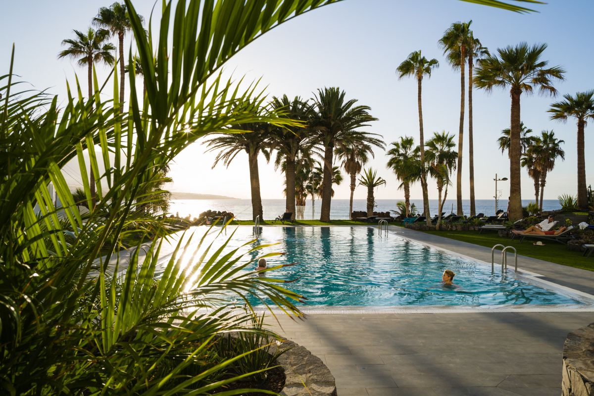 Piscina circondata da palme al tramonto a Tenerife, con vista sull'oceano.