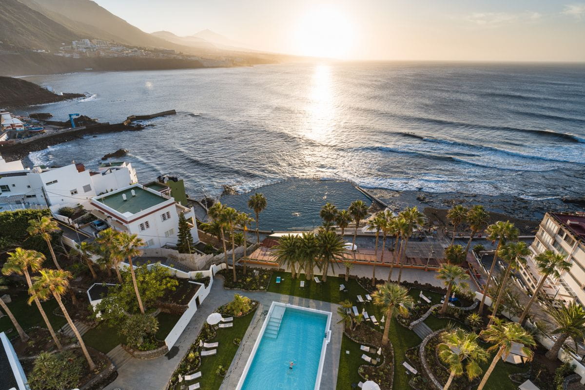 Vista aerea della costa di Tenerife al tramonto con piscina e giardini.