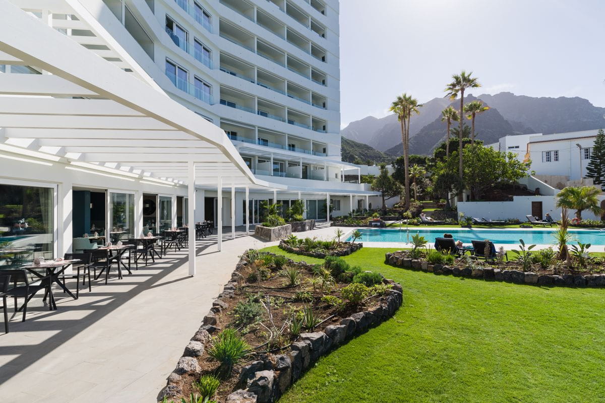 Terrazza di un hotel a Tenerife con tavoli, piscina e montagne sullo sfondo.